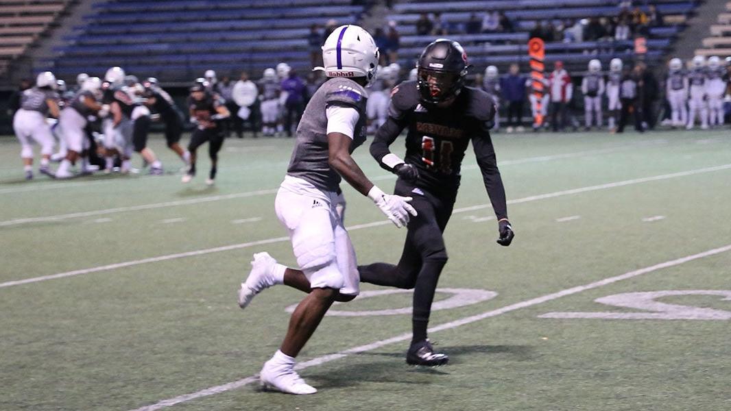 Two high school football players in uniform and helmets practice on a field